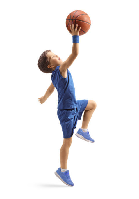 Full length profile shot of a boy in a blue jersey jumping with a basketball isolated on white background